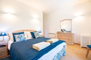 Een keurig opgemaakt bed met een blauw-witte sprei, een houten hoofdbord en een nachtkastje met een lamp.
