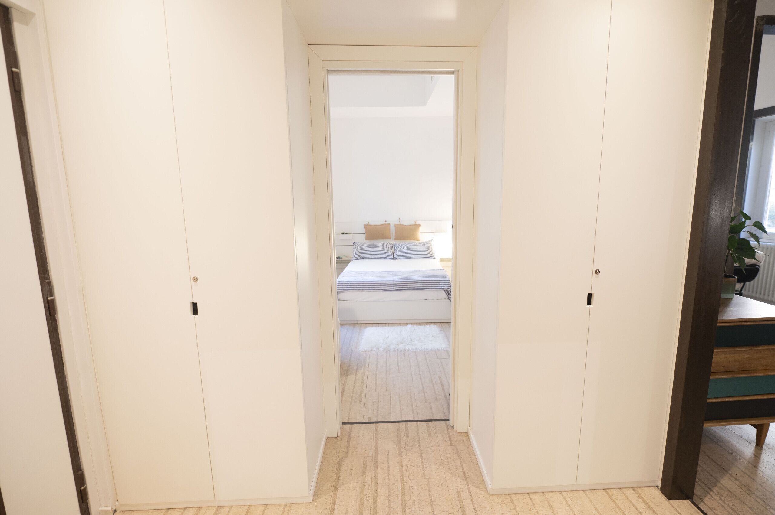 Un couloir étroit mène à une chambre à coucher qui contient un lit et une fenêtre.