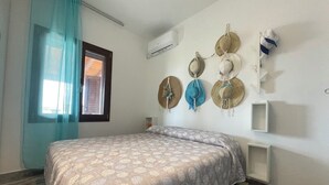 Un dormitorio con cama, ventana con cortinas, aire acondicionado y sombreros colgados en la pared.