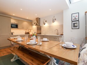 A modern kitchen with a wooden dining table set for four, equipped with glassware and plates. - Fawcett Cottage (Aldeburgh)