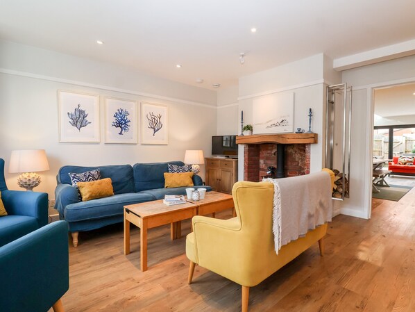 A living room with a blue sofa, yellow armchair, wooden coffee table, and a fireplace. - Fawcett Cottage (Aldeburgh)