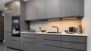 Una cocina moderna con armarios grises, una campana extractora de acero inoxidable, un fregadero y una encimera con un frutero y un hervidor.