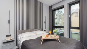 Una habitación de hotel moderna con una cama grande, una mesita de noche con una taza y un plato, una bandeja con artículos de desayuno, una ventana con vista a follaje y un panel de pared a rayas.