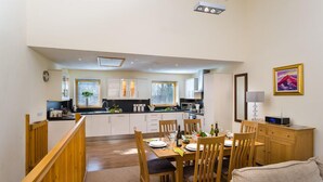 Une cuisine moderne avec des meubles blancs, un coin repas avec des meubles en bois et un tableau accroché au mur.