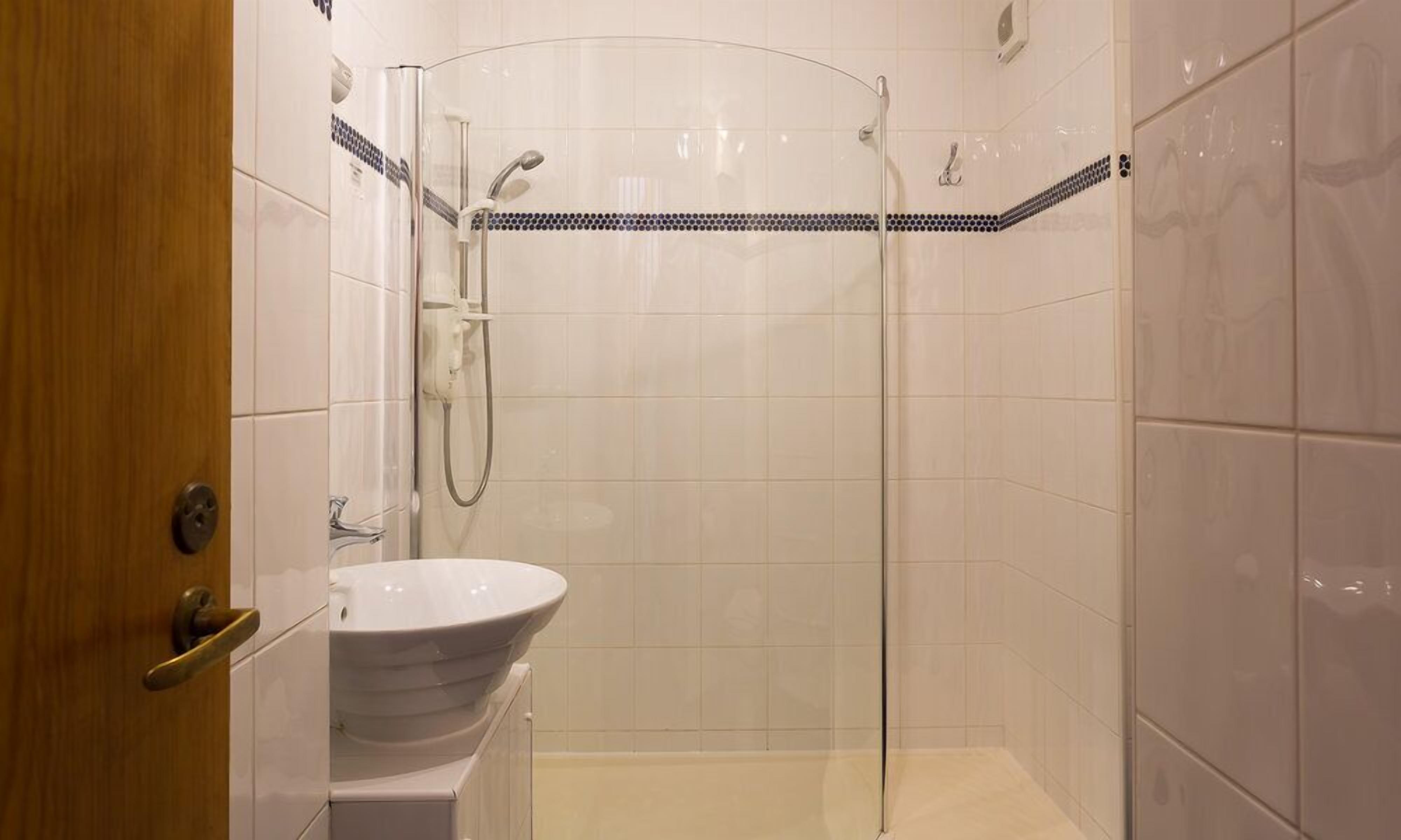 A modern bathroom with a glass shower enclosure, a white sink, and a wooden door.