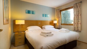 Une chambre d’hôtel avec un grand lit, deux tables de chevet avec des lampes, une fenêtre avec des rideaux et des œuvres d’art décoratives au mur.