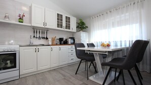 Una cocina moderna con armarios blancos, horno integrado y comedor con mesa blanca y dos sillas.