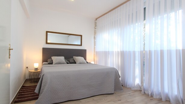 Un dormitorio con una cama, una mesita de noche, un espejo y cortinas de encaje.