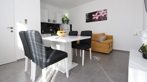 Una sala de estar moderna con comedor, que presenta una mesa blanca, sillas negras, un sofá amarillo y una planta en maceta.