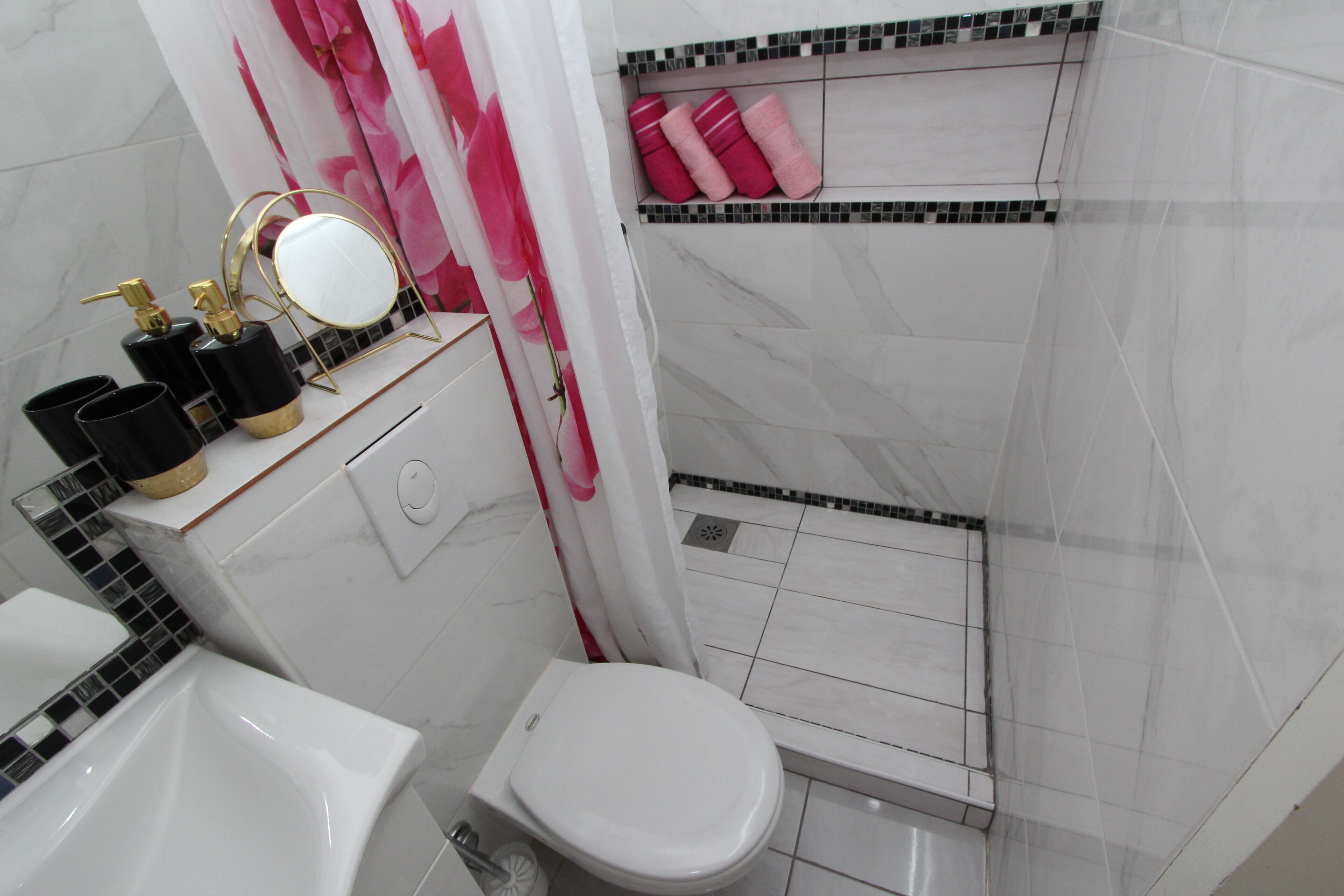 A bathroom with a white toilet, a sink, and a shower area with a tiled floor.