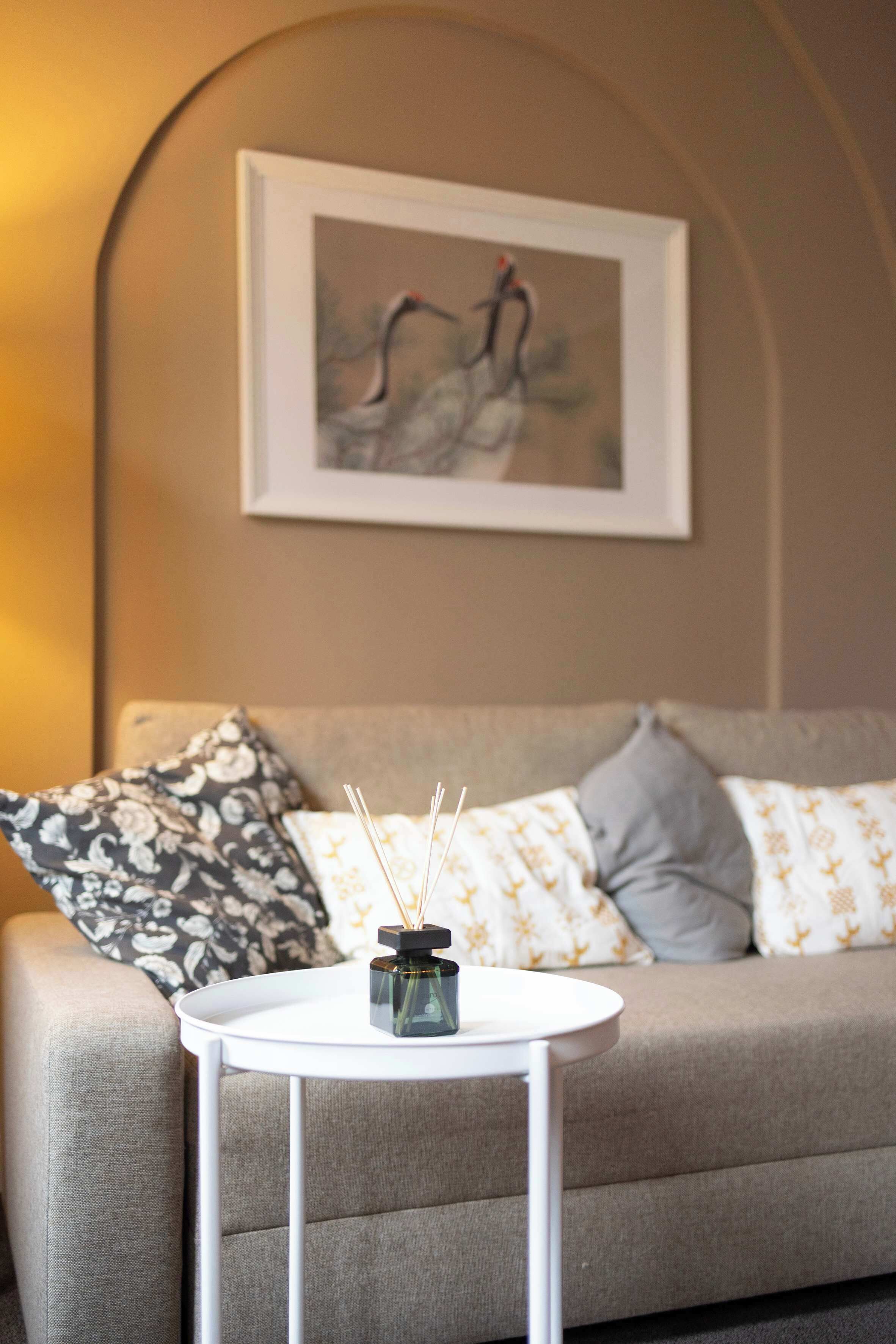 A modern living room with a grey sofa, a small white table with a decorative item, and a framed artwork on the wall.