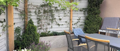 A covered patio area with a wooden pergola, a table and chairs, and a grill.
