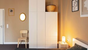 A bedroom with a bed, a nightstand with a lamp, a chair, a wardrobe, and a wall-mounted basket. - Huge apartment with Sauna and free parking (Duisburg)