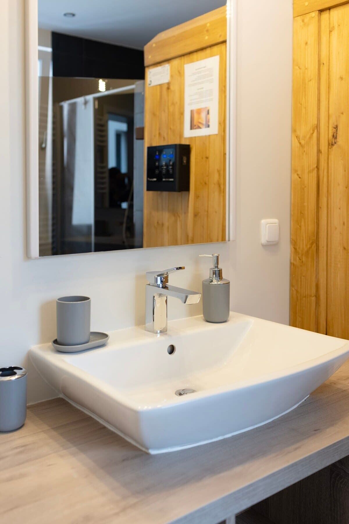 A modern bathroom with a large white sink, a mirror, and wooden paneling.