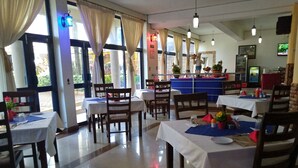 Ein Restaurant mit mehreren Tischen und Stühlen, einer Theke mit einer Auslage und einem Fernsehbildschirm.