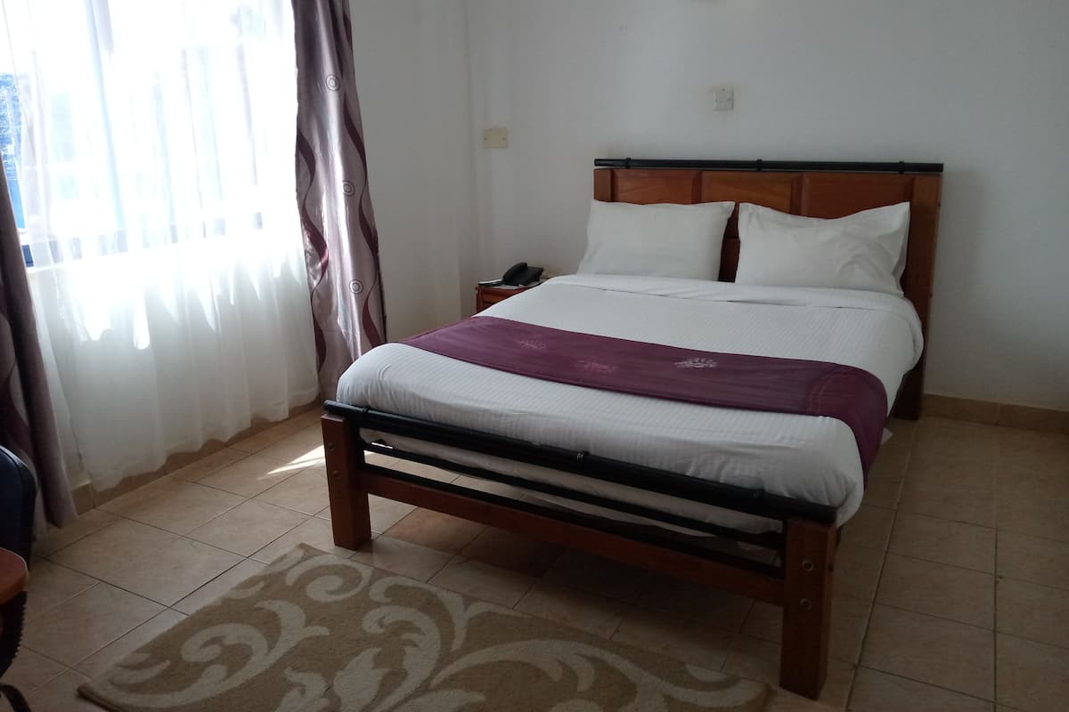 A bedroom with a bed, a nightstand, a lamp, and a window with curtains.