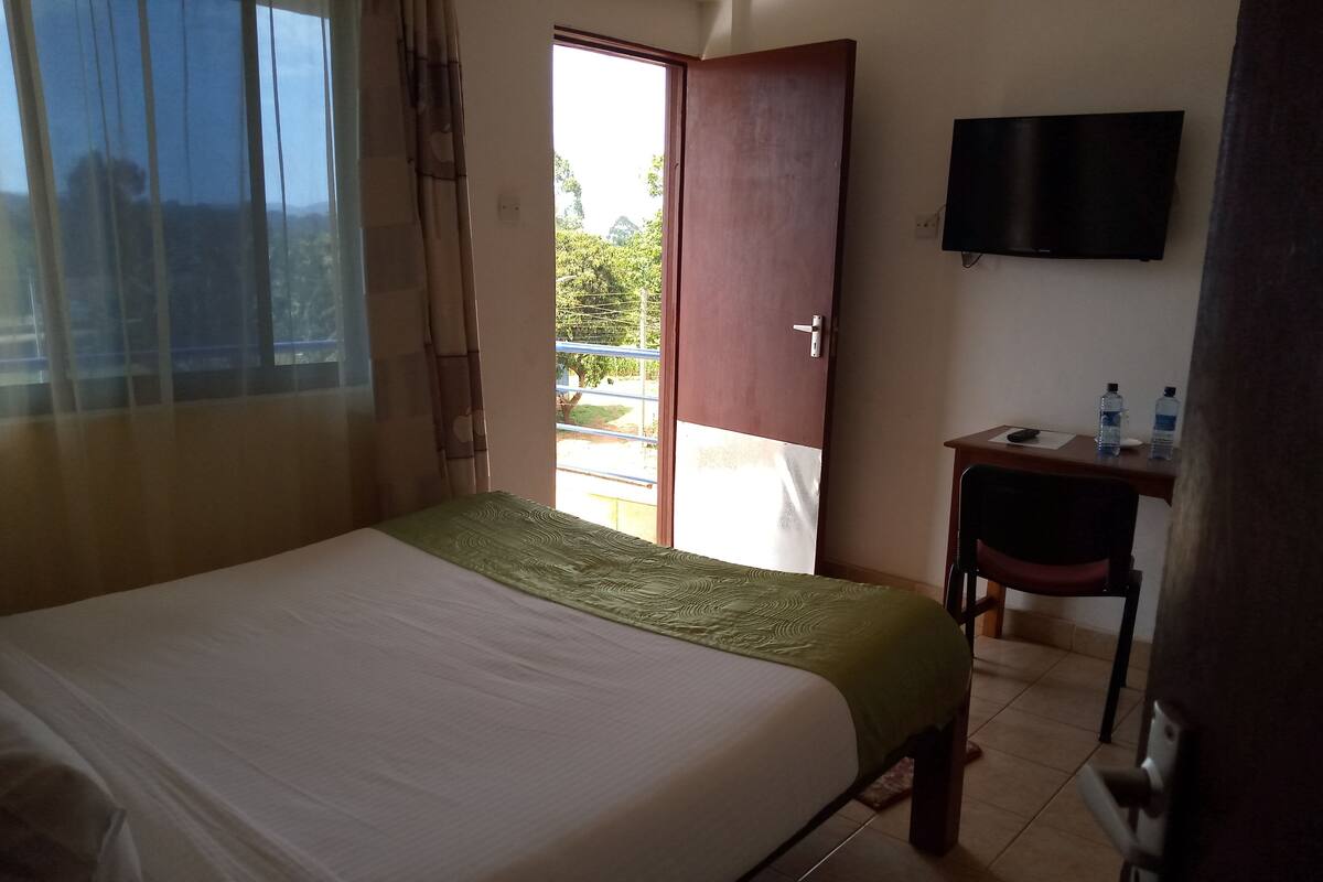 A hotel room with a bed, a desk, a chair, a television, and a window with curtains.