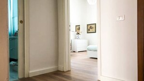 A hallway with wooden flooring leading to a room with a white dresser and a white chair. - 2 bedroom apartment in florence (Firenze)