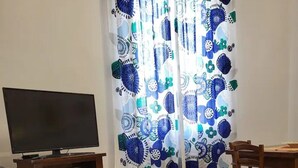 A living room with a sofa, a TV, a wooden dining table, and a patterned curtain.