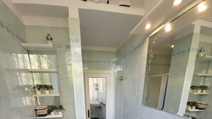 A bathroom with a bidet, a sink, and a toilet. There are shelves with plants and toiletries.