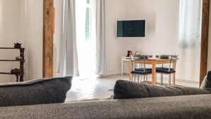 A living room with a sofa, a dining table with chairs, a TV mounted on the wall, and a window with curtains. - 1 bedroom apartment in florence (Firenze)