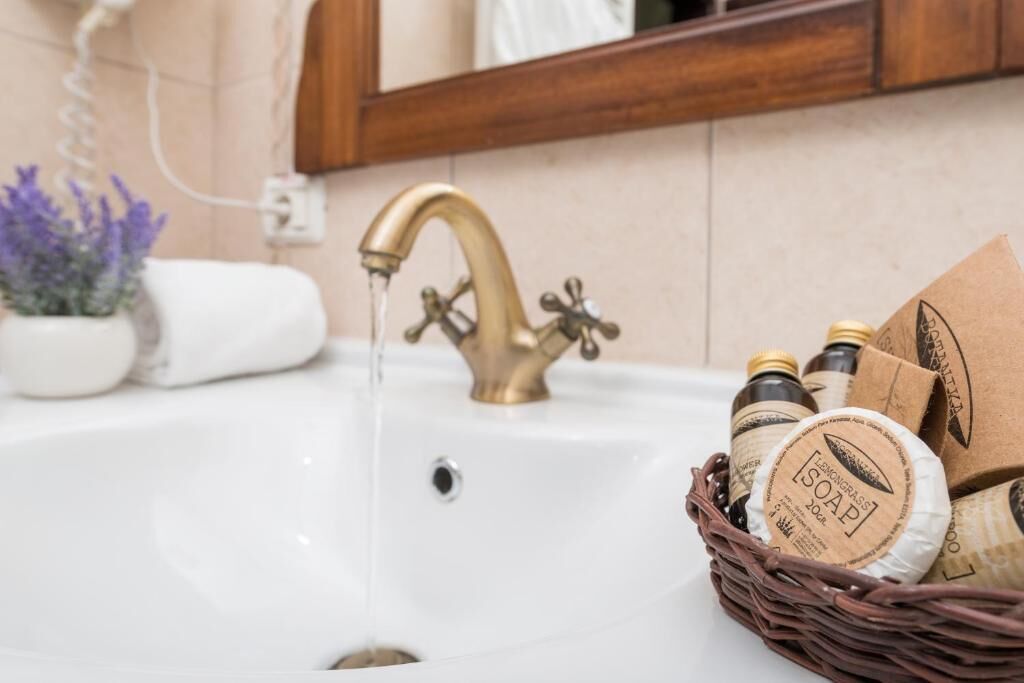 A bathroom sink with a brass faucet, a white towel, and a basket of soap bottles.