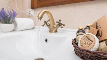 A bathroom sink with a brass faucet, a white towel, and a basket of soap bottles.