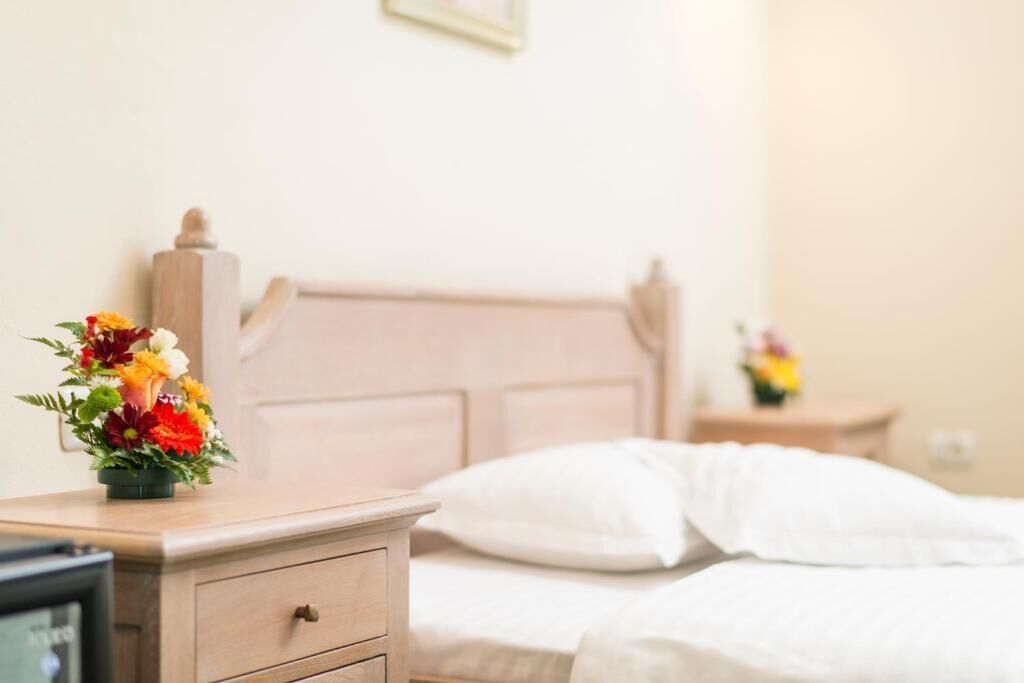 Una habitación de hotel con una mesita de noche de madera, una cama con ropa blanca y una pequeña mesa con un florero.
