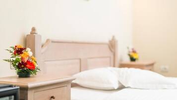 Una habitación de hotel con una mesita de noche de madera, una cama con ropa blanca y una pequeña mesa con un florero.