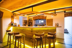 Una zona de bar con taburetes de madera, mostrador y estantes llenos de botellas.
