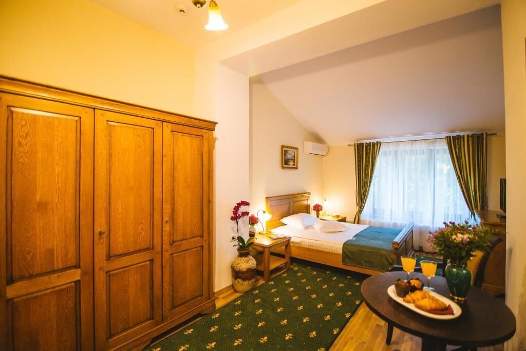 A hotel room with a bed, a bedside table with a lamp, a small table with breakfast, and a wardrobe.