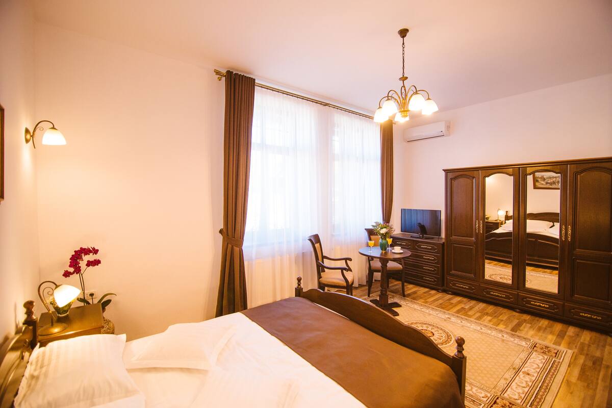 Une chambre d’hôtel comprenant un lit, un bureau, une chaise, une armoire et un lustre.