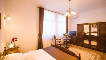 A hotel room with a bed, a desk, a chair, a wardrobe, and a chandelier.