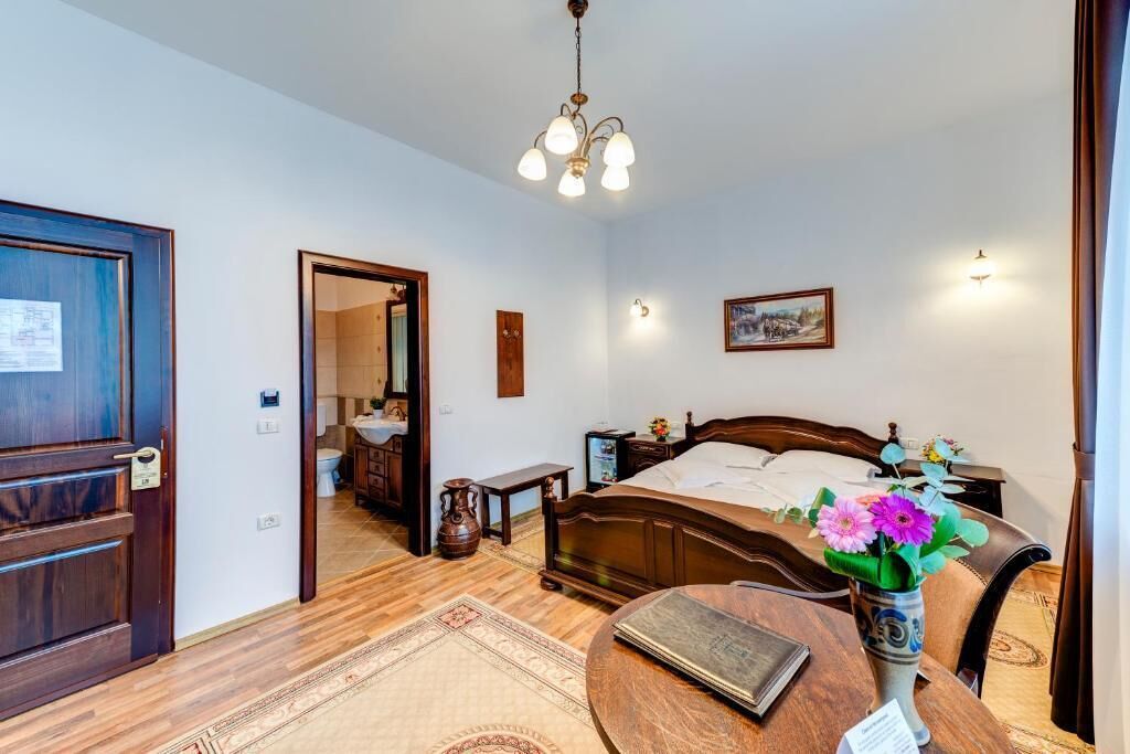 Une chambre à coucher avec un lit en bois, une table de chevet, une commode, un vase de fleurs, un lustre et une porte.