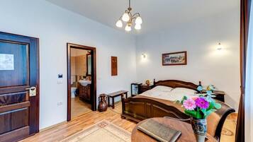 Une chambre à coucher avec un lit en bois, une table de chevet, une commode, un vase de fleurs, un lustre et une porte.