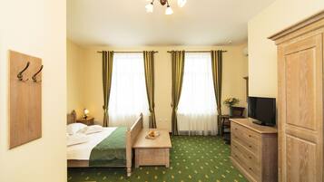 Une chambre d’hôtel avec un lit, un bureau, une commode, une télévision et des rideaux.