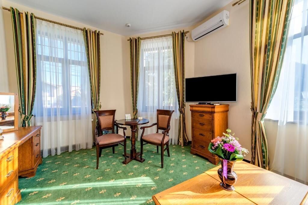 Habitación de hotel con alfombra verde, muebles de madera, un televisor y un florero con flores.