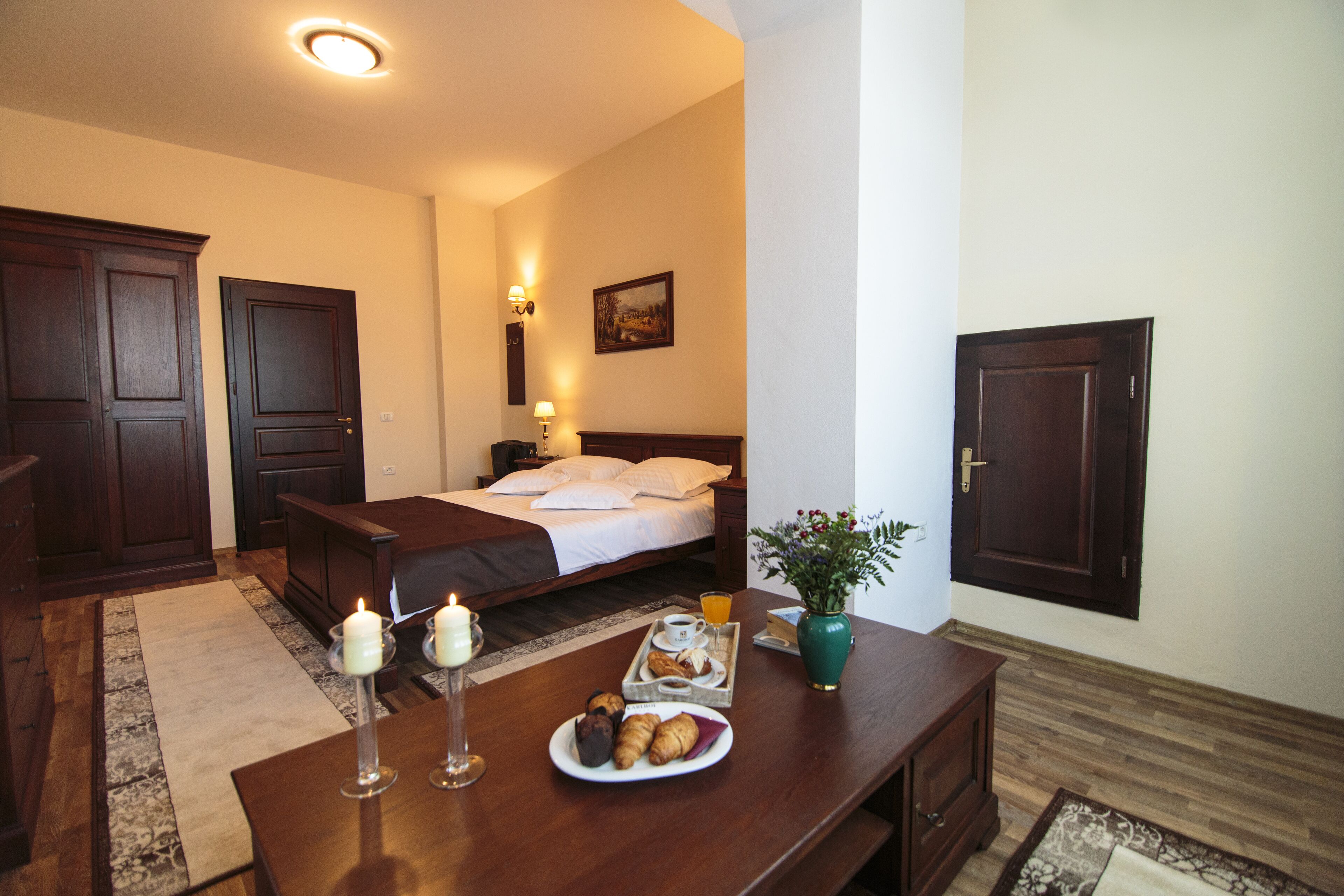 Habitació d'hotel amb llit, taula de nit i safata de petitdejuni amb pastissos.