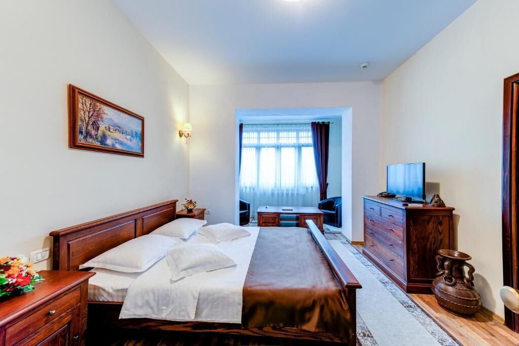 A hotel room with a large bed, a desk with a chair, a television, and a painting on the wall.