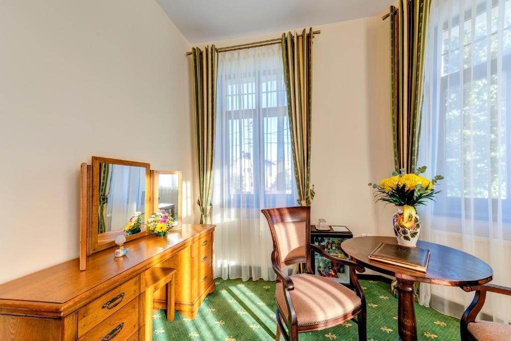 Una habitación con un escritorio de madera, una silla, una mesa redonda, un espejo y un jarrón con flores.