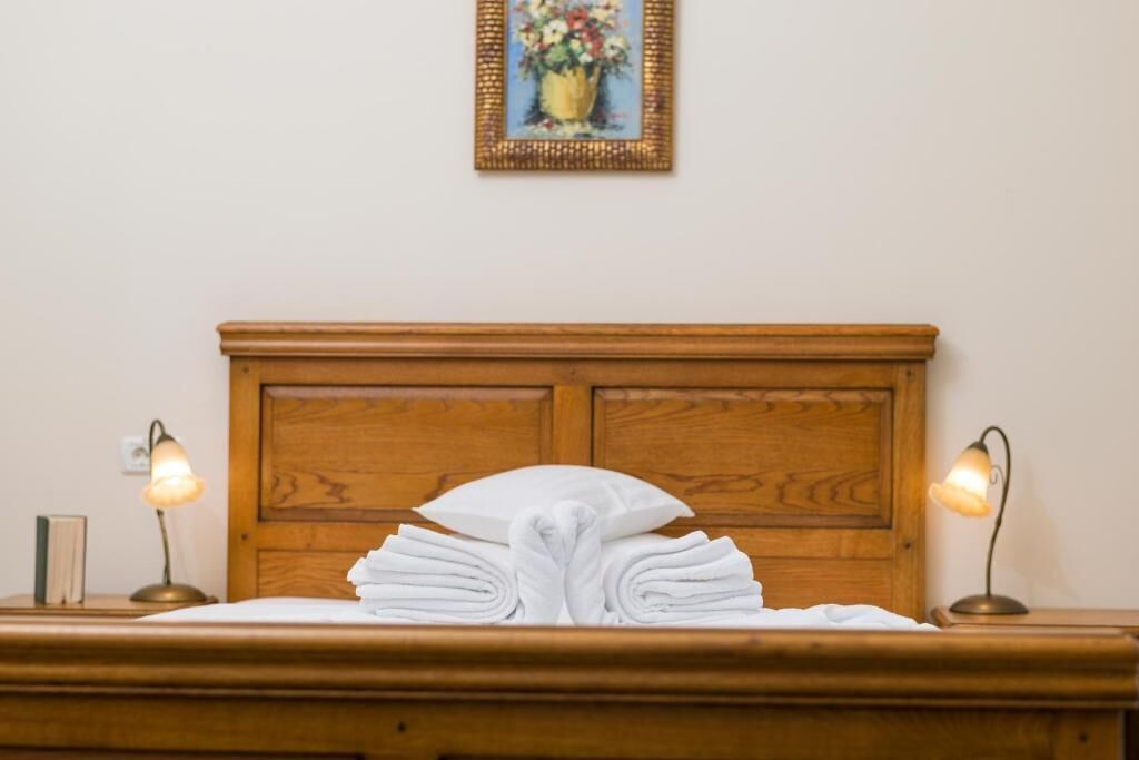Una cama bien hecha con una toalla blanca doblada en el centro, un cabecero de madera y dos lámparas de noche a cada lado.