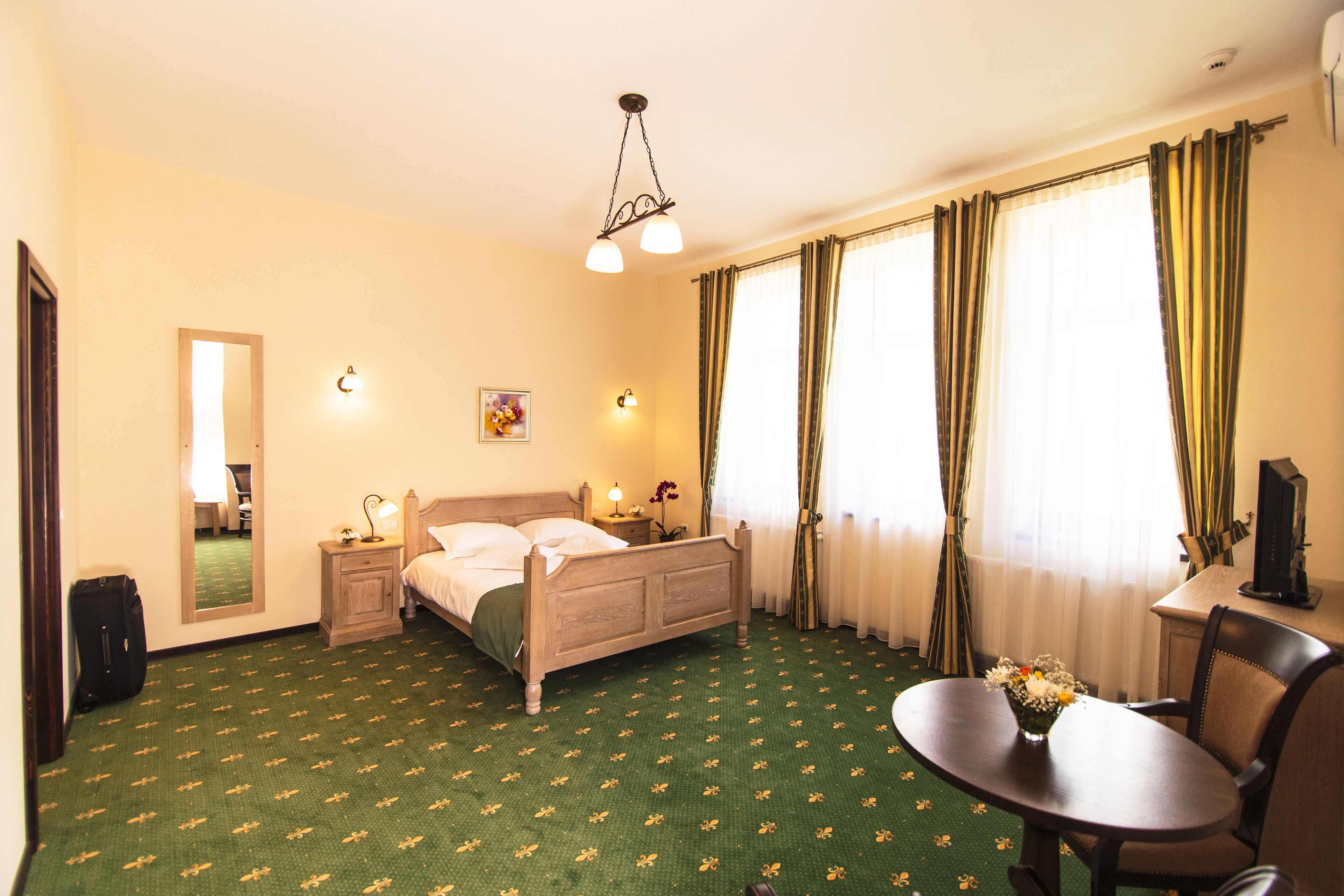Una habitación de hotel con cama, mesita de noche, lámpara y una pequeña mesa con un jarrón de flores.