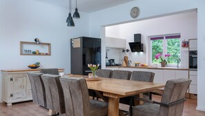 Eine moderne Küche mit Essbereich, ausgestattet mit einem Holztisch und Stühlen, einem Kühlschrank und einem Fenster mit Blick ins Grüne.