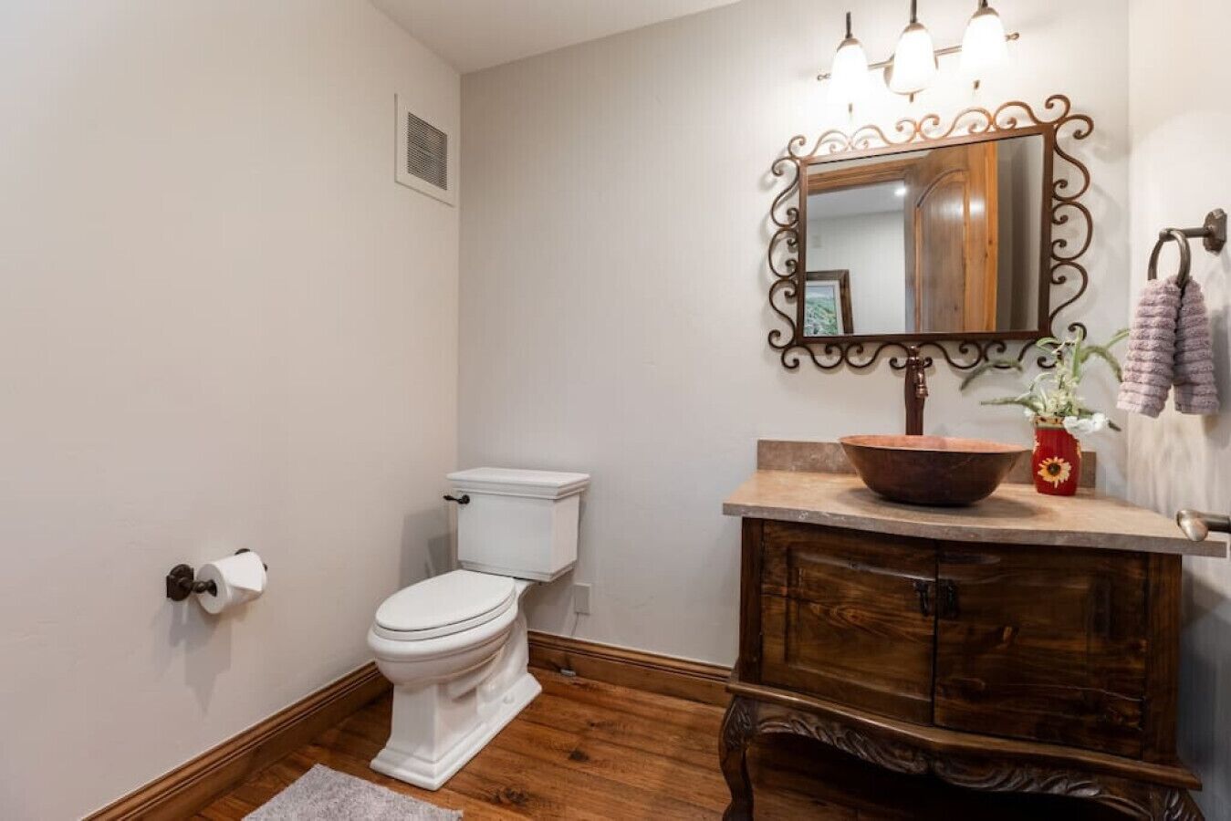 A bathroom with a white toilet, wooden vanity, and a large mirror with a decorative frame.