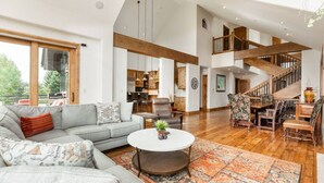 Ein geräumiger Wohnbereich mit einem grauen Sofa, einem runden Couchtisch und einer Treppe, die zu einer oberen Ebene führt.