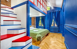 Ein Zimmer mit Etagenbett, einem Holzboden im Fischgrätmuster und einer Treppe, gestrichen in Rot, Weiß und Blau.