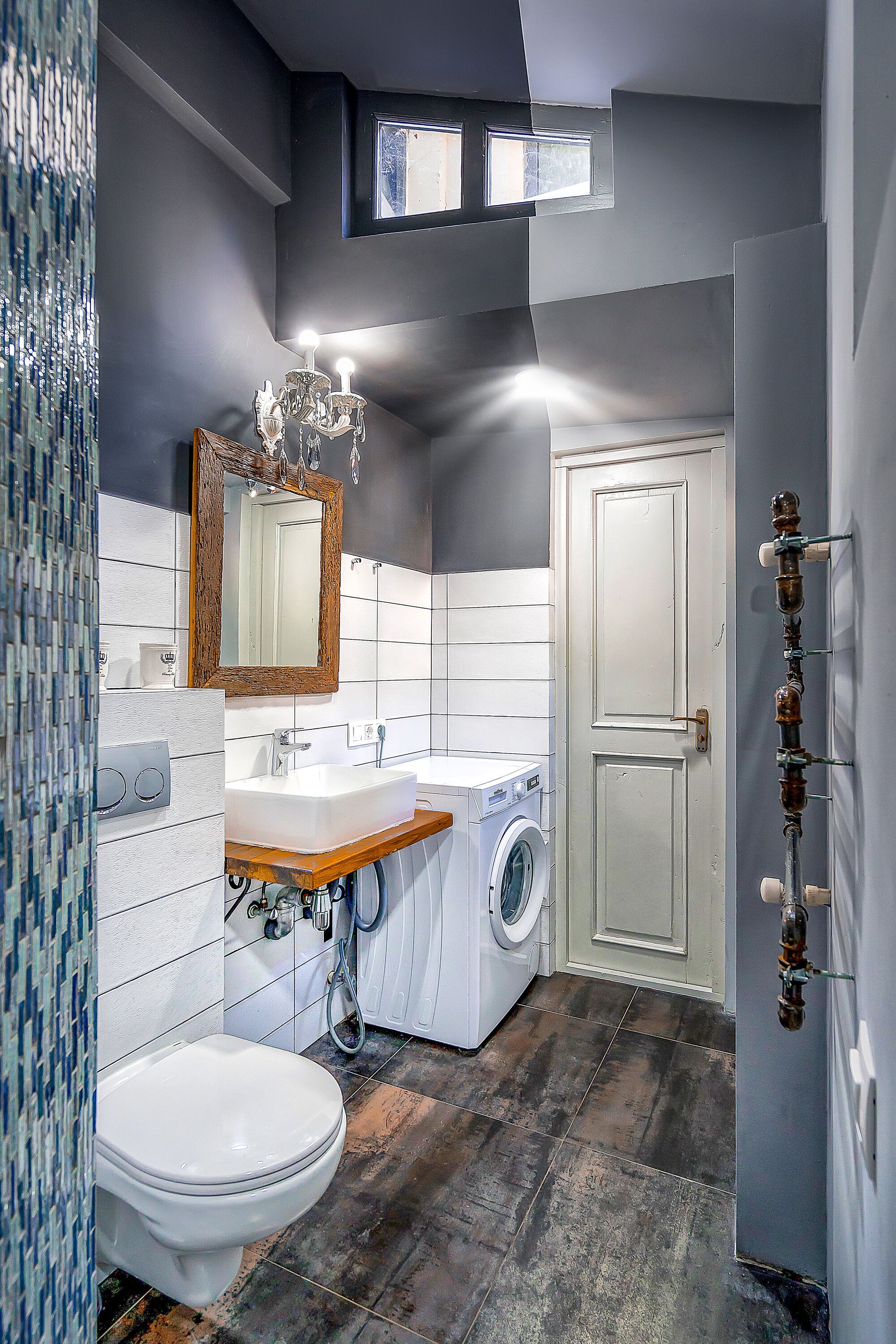 A bathroom with a white toilet, a sink, a mirror, a chandelier, a washing machine, and a door.