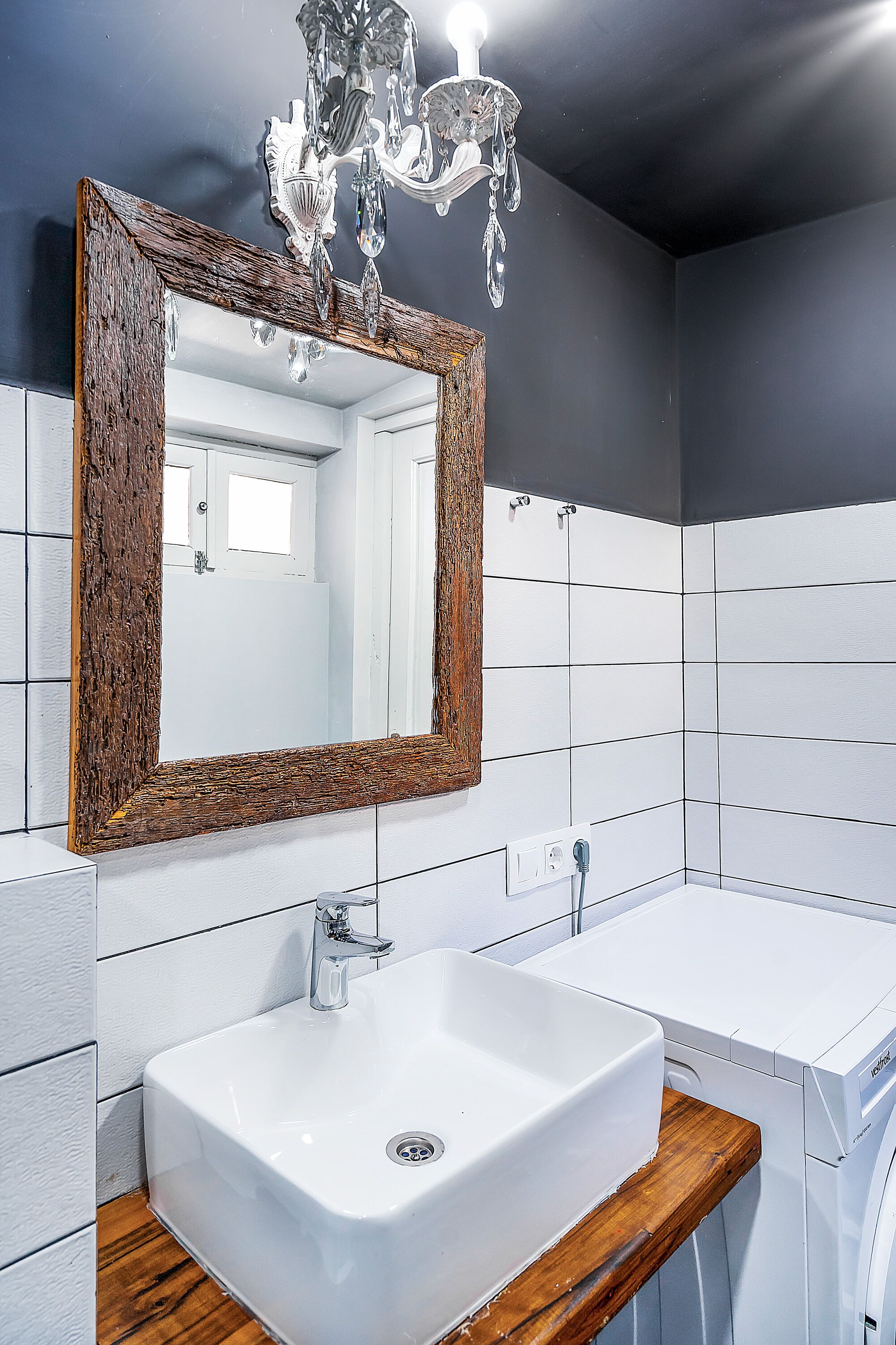 Un baño con tocador de madera, lavamanos blanco y espejo con marco de madera.