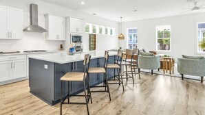 A modern kitchen with white cabinets, a large island with bar stools, and a dining area with a view of the outdoors. - Inlet Beach! Sleeps 10, 4 BR/3.5 BA , Pool & just minutes to the beach, Rosemary area and 30Avenue! (Inlet Beach)