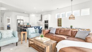 A modern living room with a sofa, armchair, and coffee table, a kitchen in the background, and a dining area with chairs. - Inlet Beach! Sleeps 10, 4 BR/3.5 BA , Pool & just minutes to the beach, Rosemary area and 30Avenue! (Inlet Beach)